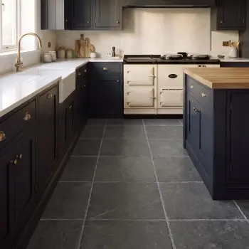 Modern country kitchen with large dark grey stone-effect floor tiles, charcoal cabinetry, white range cooker, wood worktops and brass fittings.