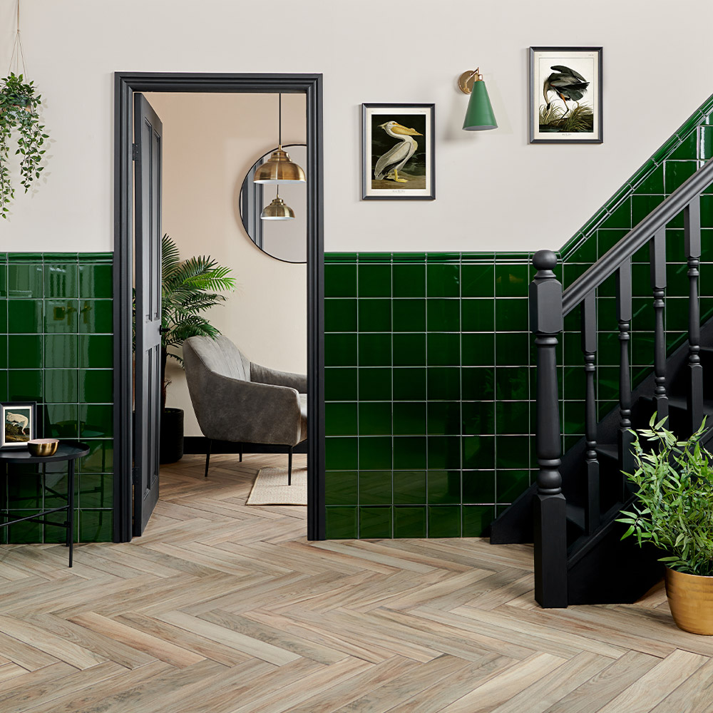 Capsule Victorian green square ceramic tiles with moldura dado border and neutral light painted walls with brown natural wood effect herringbone flooring 