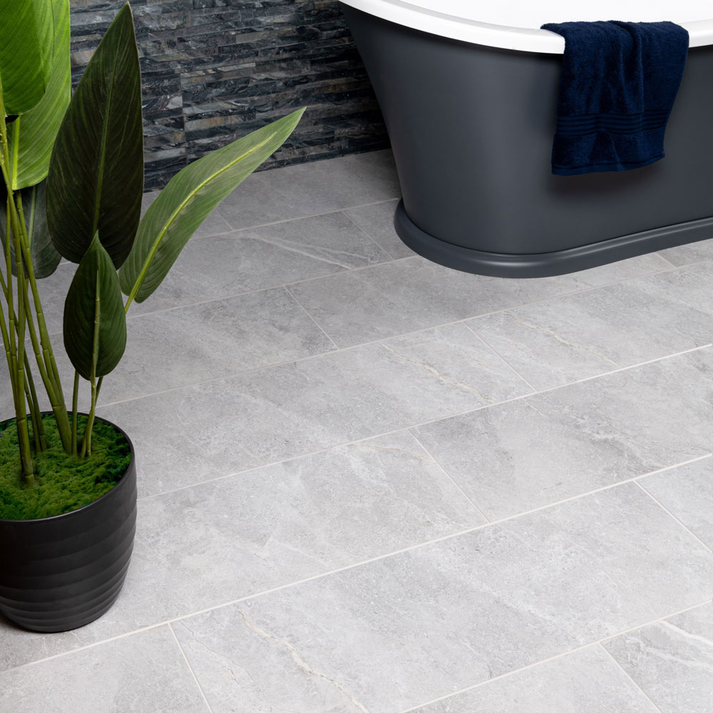Grey rectangular marble effect floor tiles with split face brick grey tiles on wall. Traditional grey bath with large standing plant. 