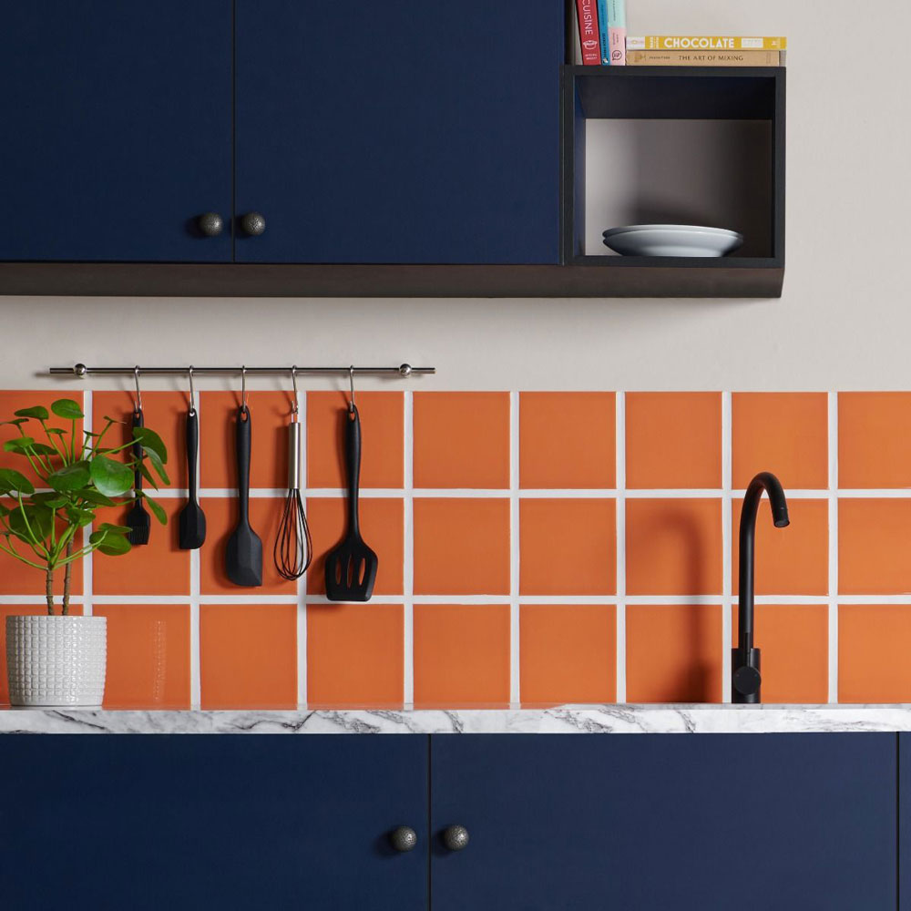 Kitchen colour idea shows orange splashback tiles with navy blue cabinetry and black hardware. 