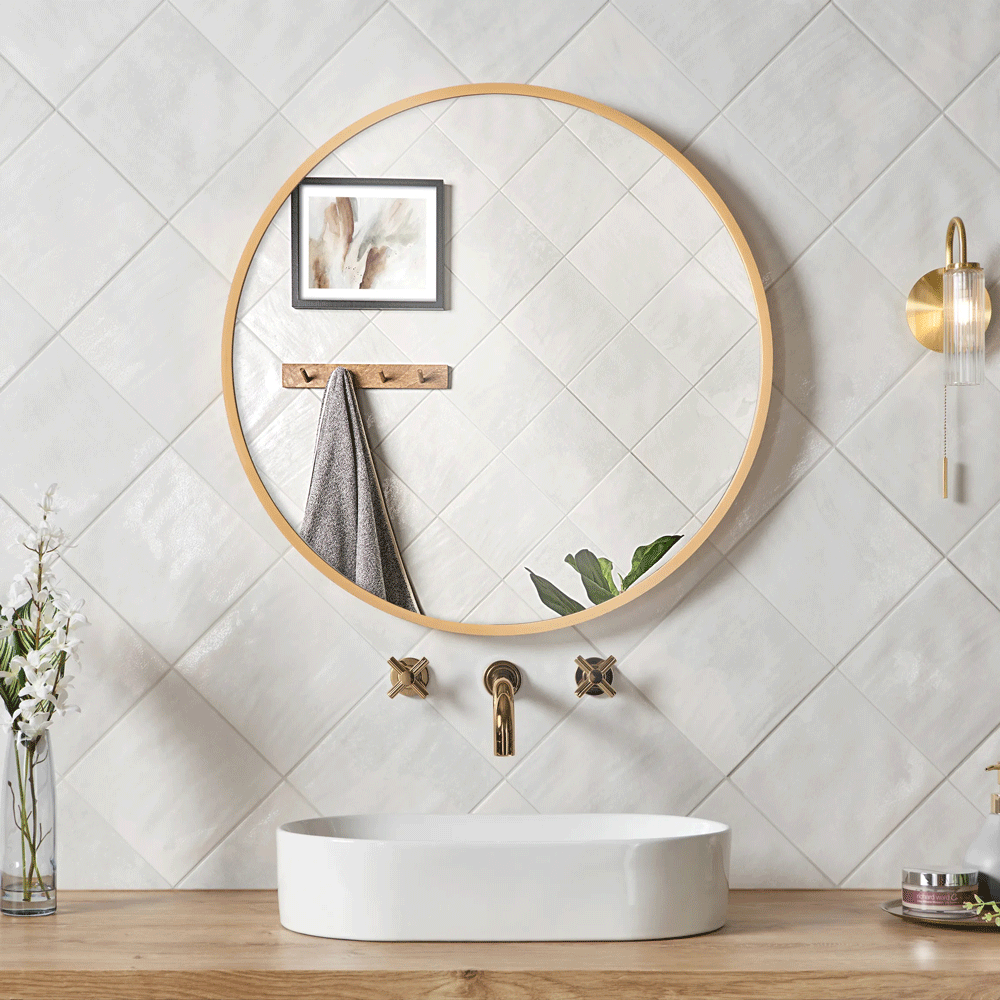 Simple white tiles used across sink area with white counter top basin and gold hardware. Wall mounted wood framed mirror adds texture. 