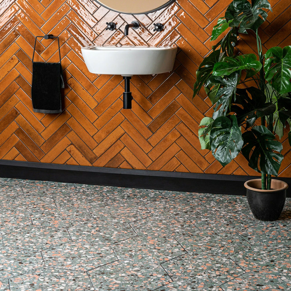 Green terrazzo floor tiles with vibrant orange brick shape wall tiles in geometric designs. 