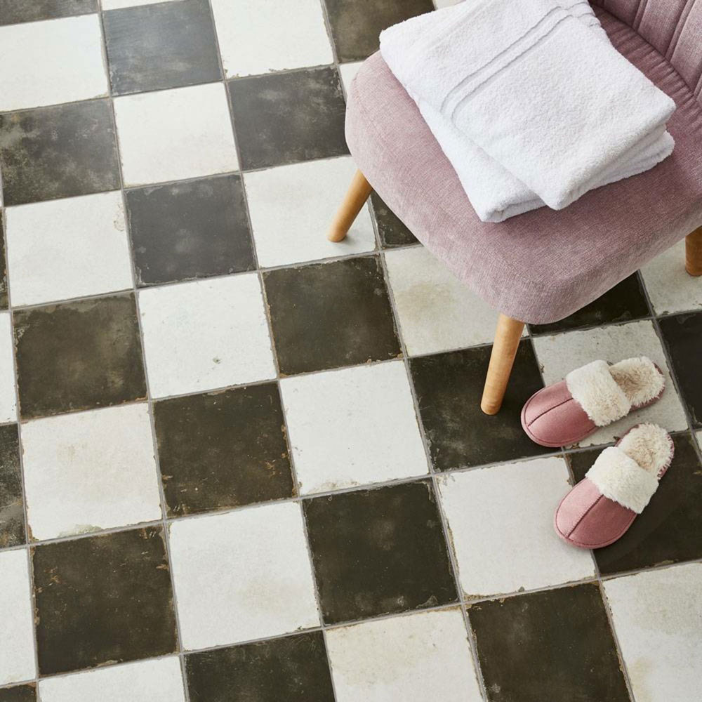 Rustic weathered effect black and white chequer floor tiles across floor with pink chair and slippers to accessories.