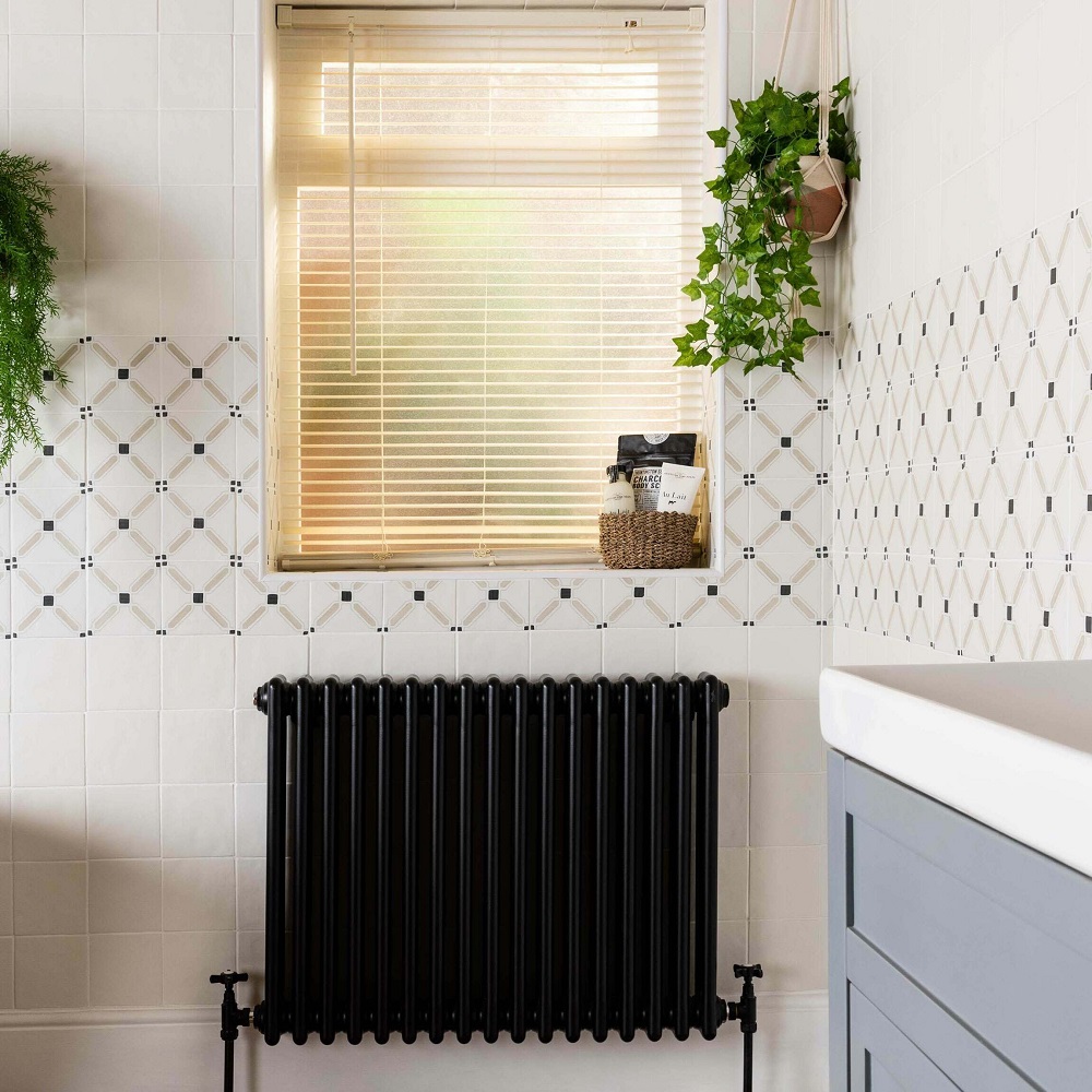 Neutral patterned tile bordering bathroom scheme with beige tones, black traditional radiator and plants throughout. 