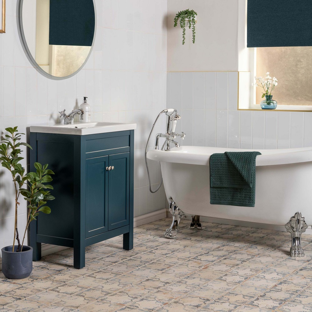 Traditional freestanding bath with claw feet, in Moroccan bathroom with weathered patterned floor tile and navy blue vanity basin unit. 