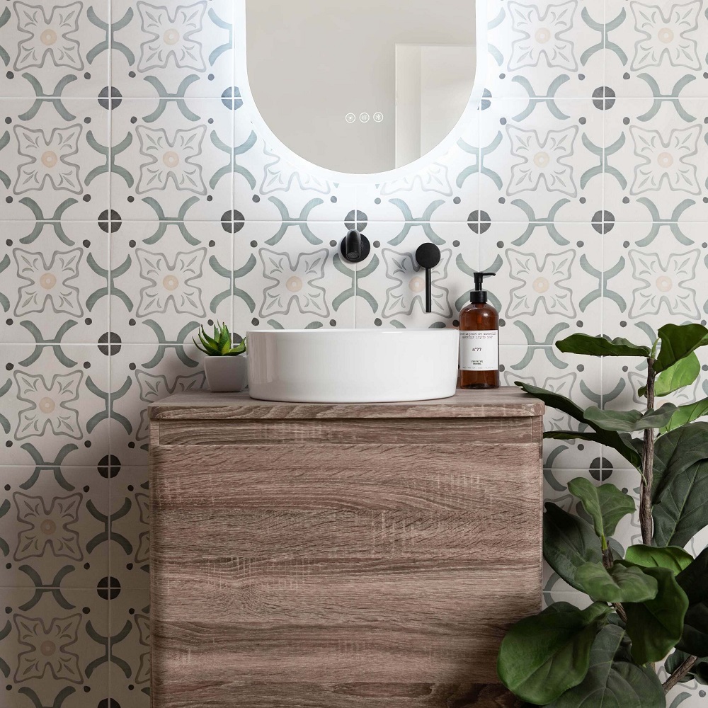 Pastel green and grey floral tiles across splashback of bathroom sink area with wooden vanity unit. 