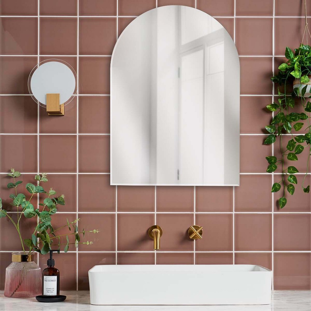 Muted pink square tiles across splashback of bathroom with gold hardware and plants to accessorize.
