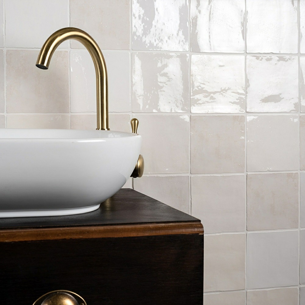 Small white square tile size across splashback in bathroom scheme with white basin and gold taps.