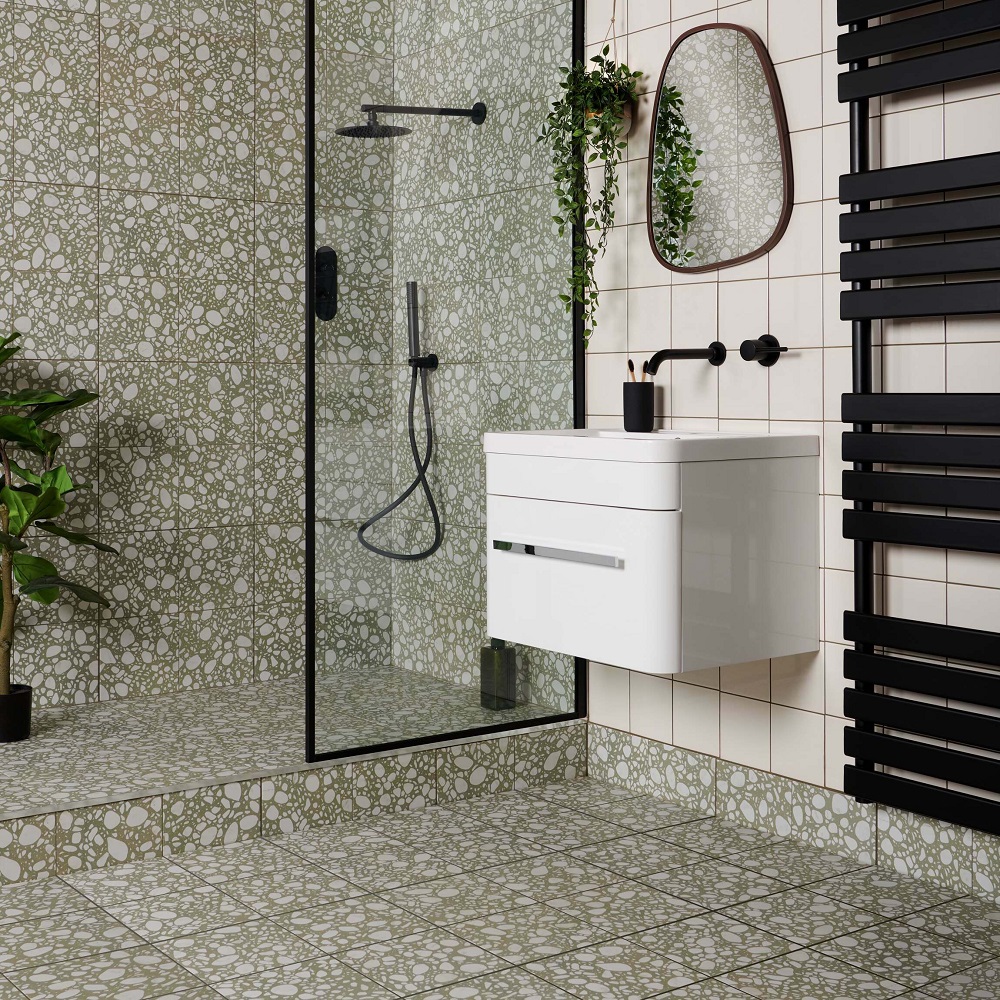 Pastel green terrazzo effect tiles across shower and floor space in white bathroom with matt black accessories. 