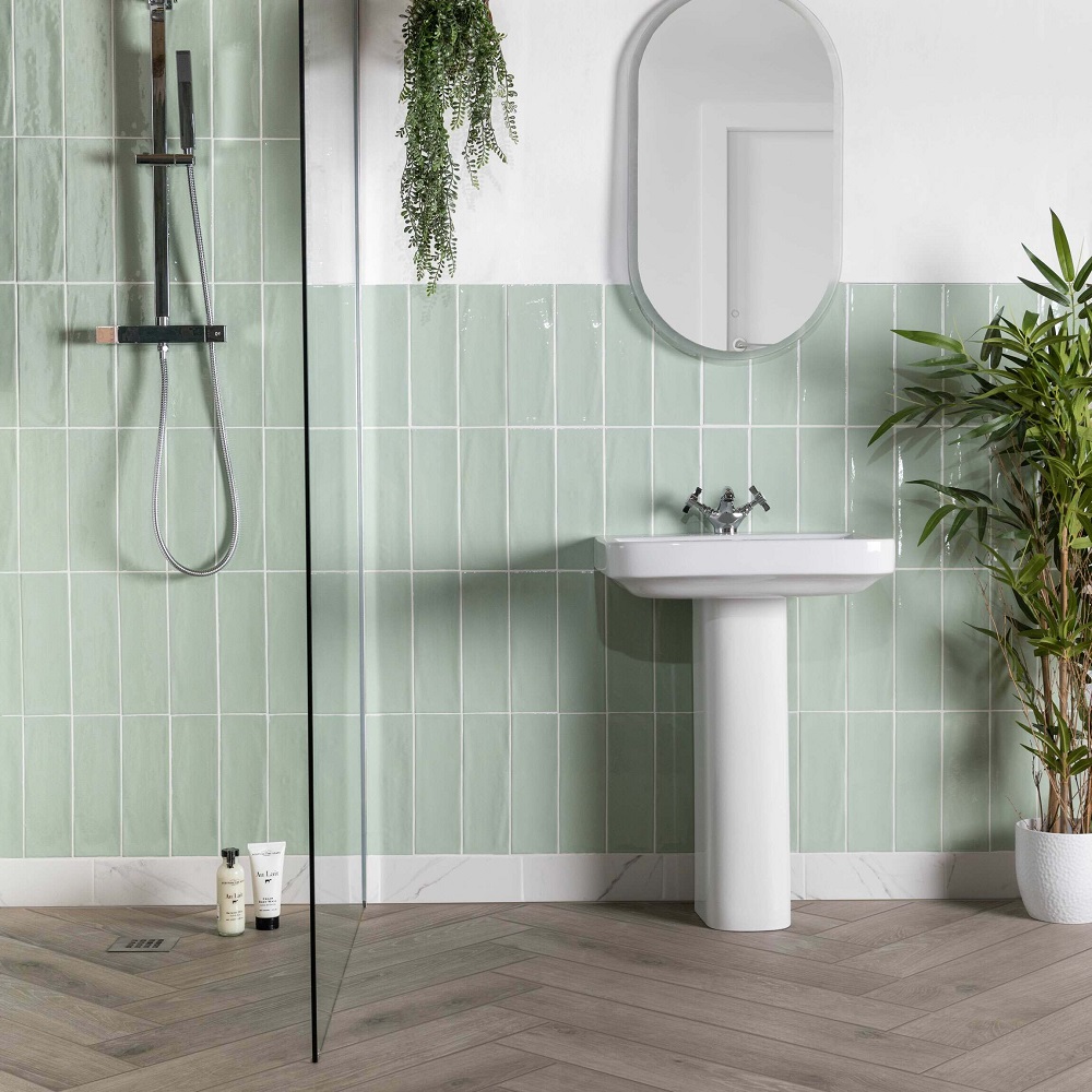 Pastel green brick shape wall tiles across shower and splashback in bathroom with wood tile flooring. 
