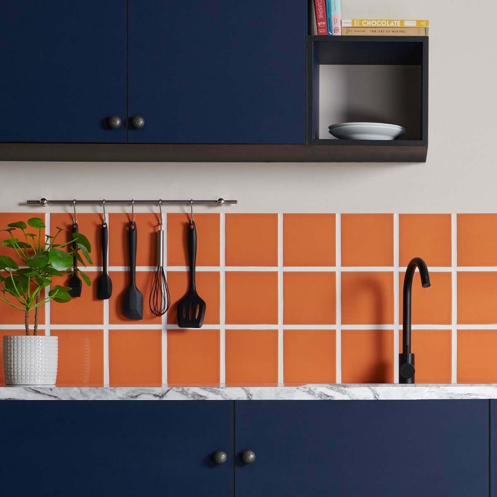 Vibrant orange kitchen splashback with navy blue kitchen cabinets and matt black accessories. Wall mounted hanging rail above kitchen splashback.