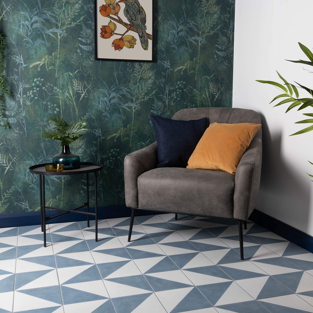 Geometric white and blue floor tiles with detailed leafy wallpaper and grey chair styled in a living space. 