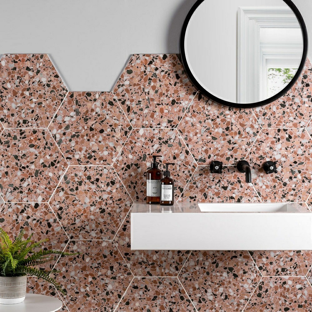 Pink terrazzo effect hexagon tile for pink interior ideas, featuring white wall mounted sink and matt black taps creating contemporary look.