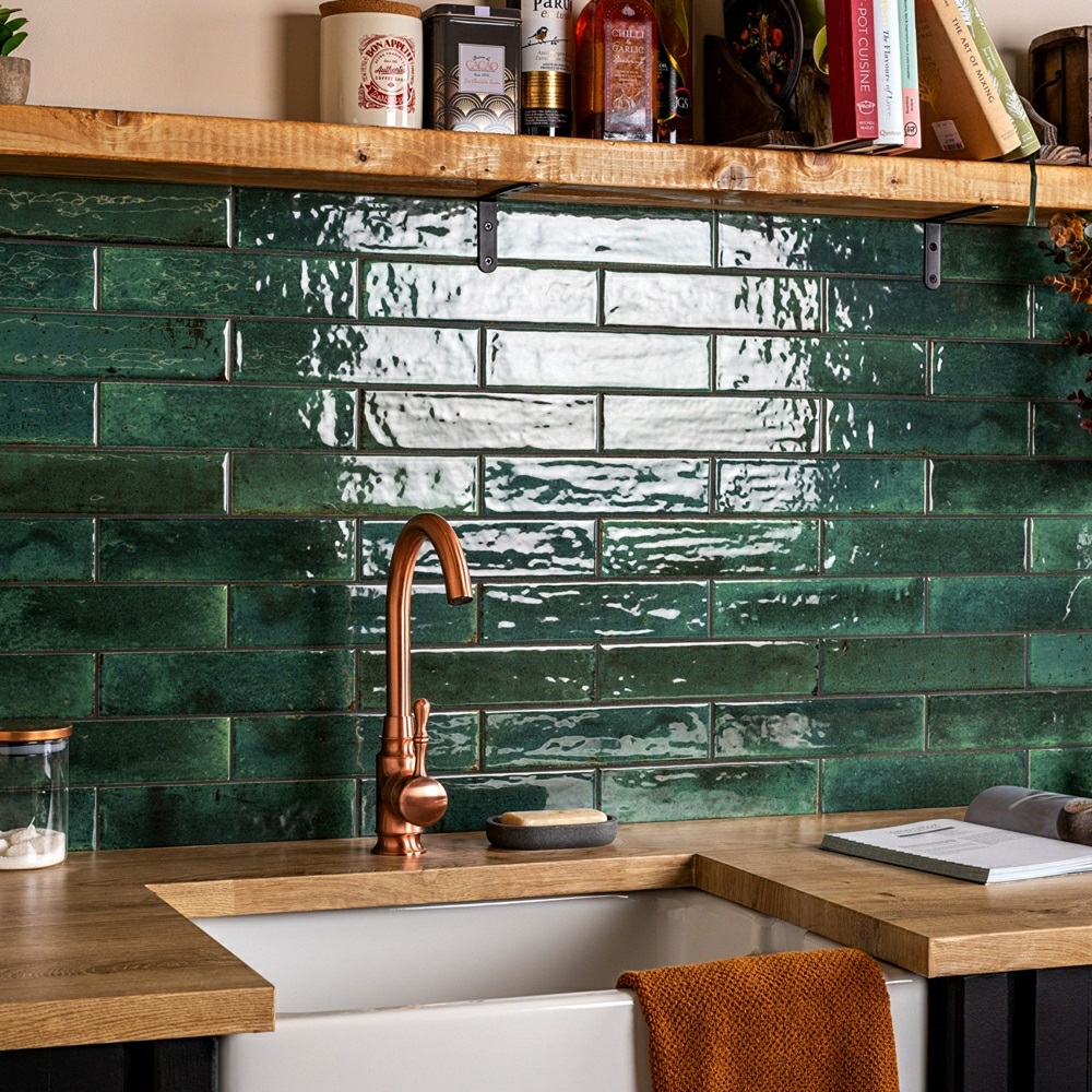 Dark green gloss brick tiles across kitchen splashback with copper tap and wood surfaces around sink space.