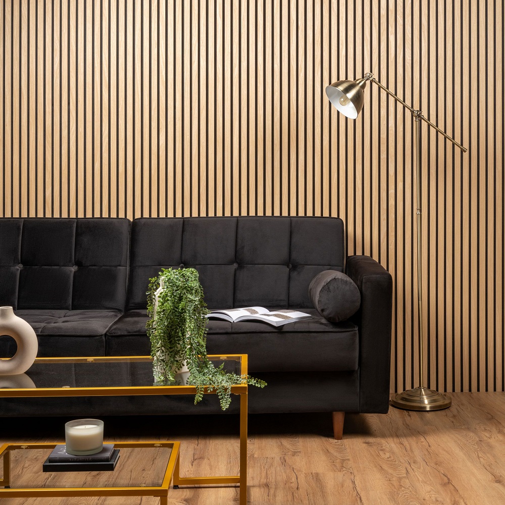 Dark velvet sofa in living room space with light wood slat wall panels across wall behind sofa, coffee table with plants and accessories on.