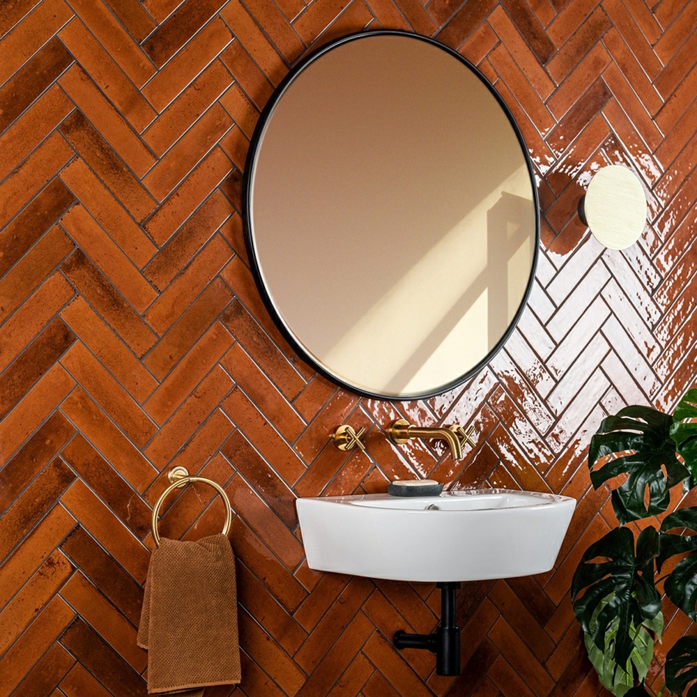Burnt orange wall tiles in herringbone ;ayout in bathroom with gold accents and wall mounted basin.