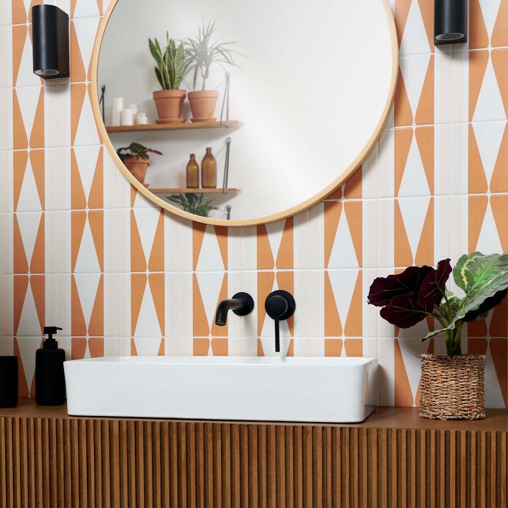 Bathroom colour ideas are reflected in this bathroom featuring terracotta geometric tiles and a natural wood vanity. The modern square basin and matt black taps add a sleek touch, while a round mirror and greenery introduce a cosy feel. 