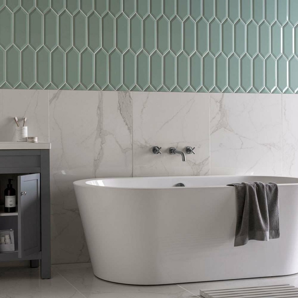 A bathroom with a sleek white oval bathtub, marble wall tiles, green geometric tiles across upper wall with a dark green vanity unit and white sink.