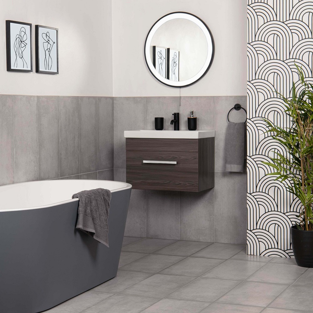 Modern bathroom with grey floor and wall tiles, a freestanding bath tub, dark wood vanity, and black accessories. The circular mirror and monochrome art add sophistication, while the pattered wallpaper and green plant introduce texture and life to the space. 