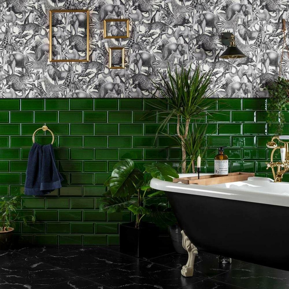Bathroom colour ideas are reflected this chic bathroom that features a striking contrast between the upper walls, with lively monochrome animal print wallpaper with emerald green wall tiles below. Centrepiece is an elegant freestanding bath with claw feet, paired with gold features. Greenery adds a fresh touch to the space.
