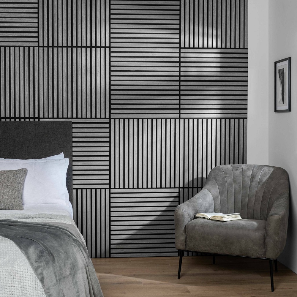 Modern bedroom with acoustic wood slat wall panels in a geometric pattern, featuring a plush grey armchair and a cosy bed with neutral linens. 