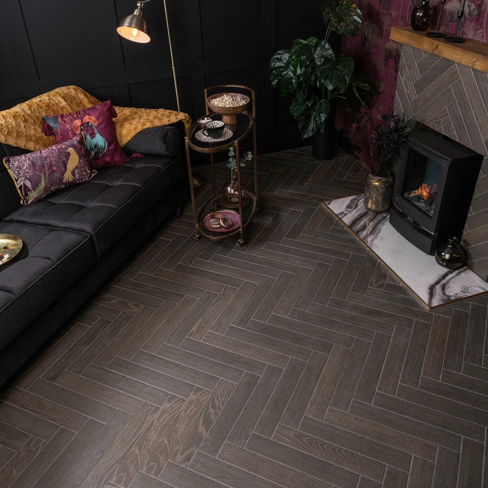 Bohemian chic living room boasting dark wood effect tiles laid in a herringbone format, creating a stunning contrast with the plush black sofa and vibrant mustard throw, highlighted by a cosy log burner and eclectic decor. 