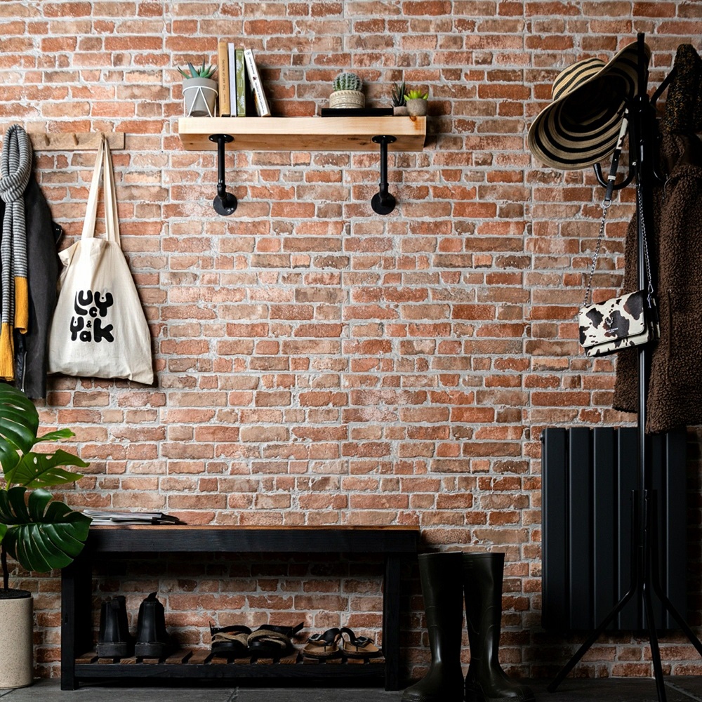 An effortlessly rustic hallway showcasing brick effect tiles that deliver a touch of industrial charm. The natural wood shelf and black metal brackets serve as a minimalist display for books and greenery. Below, a sleek black bench doubles as a shoe organiser, maintaining a clutter free space. Coats and bags hang neatly on the wall mounted hooks, while a pair of welly boots stands ready for outdoor adventures, adding functional yet stylish hallway storage solutions. 