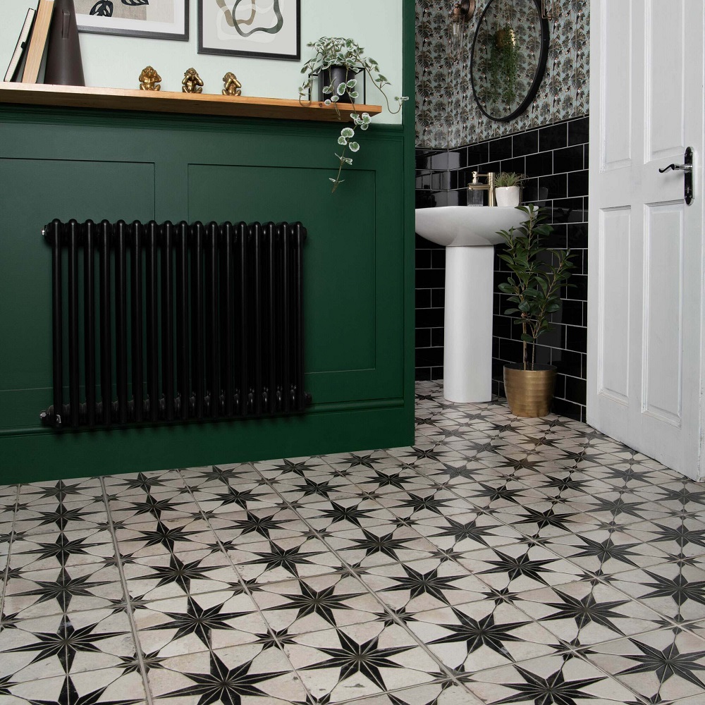 A chic and inviting hallway featuring Cinders Lux Star pattern tiles. The geometric star design in black and white exudes timeless elegance, perfectly complementing the bold, forest green wainscoting. Black subway tiles add depth to an adjoining downstairs bathroom, harmonising with a traditional black radiator. A pedestal sink, brass accents and indoor plants infuse the space with a fresh, contemporary vibe, ideal for welcoming guests with style. 