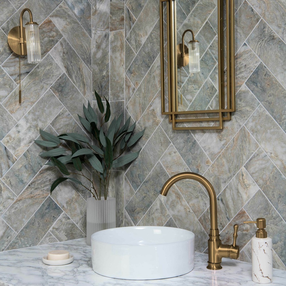 A luxurious bathroom corner featuring Passion Onyx Pear wall tiles with intricate veining in green and white hues, laid in a herringbone pattern to act as wallpaper alternative. The marble-patterned soap dispenser, and a small, round dish. Adding a touch of greenery, a vase with silvery eucalyptus leaves sits gracefully, enhancing the bathrooms opulent and tranquil ambiance. 