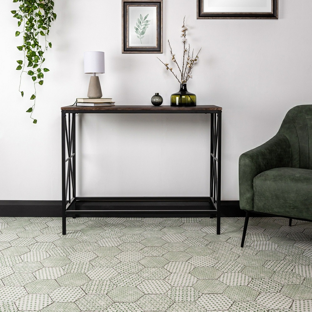 A tranquil and stylish hallway space that harmonizes Souk Green patterned tiles with soft wall tones for a refreshing, modern look. The geometric design of the tiles adds a touch of artisanal charm, while the olive green velvet chair introduces a splash of luxury and comfort. A sleek console table with a dark wood top and black metal frame offers minimalist appeal, adorned with a contemporary lamp and decorative vases. Botanical prints and cascading indoor plant contribute to the calm, nature inspired aesthetic of the hallway, creating a welcoming and peaceful entryway. 