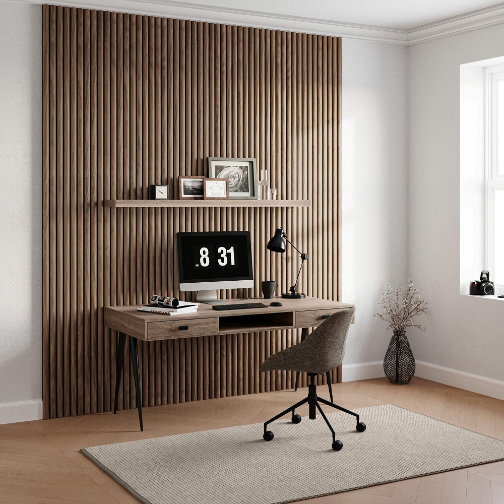 A home office setup with an autumn brown vertical panel wall backdrop. A wooden desk with an integrated shelf holds a computer displaying a large clock interface, alongside framed photos and a classic black desk lamp. An ergonomic char in tweed fabric, a textured area rug, and a vase with dried branches complete this functional yet stylish workspace. 
